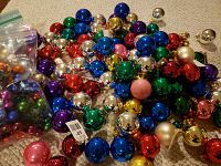 Large pile of assorted shiny glass Christmas ball ornaments in various colors and sizes, some loose scattered on carpet