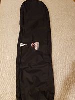 Full view of black snowboard bag laid flat on carpet showing general shape and zipper.