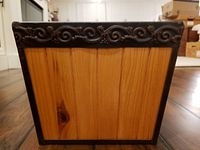 Front view showing vertical wooden panels and metal frame with decorative ornate metal band along top edge.