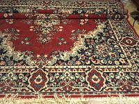 Rolled section showing central medallion pattern and floral border of red oriental styled rug.