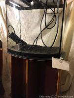 Curved front aquarium on wooden stand with black substrate inside and filter attached.