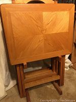 Four oak tray tables nested in a matching holder, showing wood grain pattern on top and sturdy holder frame.
