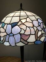 Close-up photo of Tiffany style table lamp shade showing floral stained glass pattern in pastel colors including white, lavender, purple, and blue.