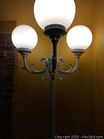 Close-up photo of the outdoor light fixture illuminated, showing the three white globe lights and decorative metal arms.