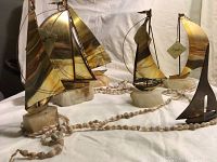 Photo showing 5 numbered brass and onyx sailboats on rounded onyx bases, a small solid brass sailboat, and a shell necklace arranged on a white cloth background.