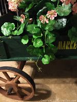 Close-up of one wooden spoked wheel and part of the green cart body showing texture and materials.