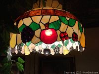 Photo showing lit stained glass hanging lamp with illuminated fruit pattern in red, yellow, green, and purple colors.