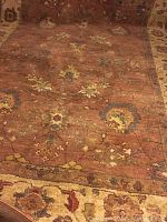Close-up of the rust-colored rug showing floral and ornamental patterns in yellow, cream, and brown tones.
