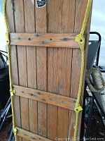 Photo of wooden toboggan showing vertical slats, horizontal wood reinforcements, and yellow rope handles.