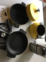 Photo showing the electric multi-pot set with sauté pan, fondue pot, and simmer pot in yellow and black colors, placed on a white background with the power cord visible.