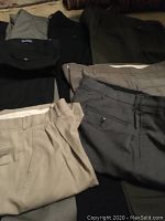 View of several pairs of men's pants in assorted colors and styles, folded and laid out, showing pockets, waistbands, and belt loops.