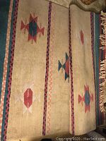 Full view of western style hand crafted area rug with beige base and dark red, green, and tan geometric patterns, showing the design and condition.