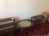 Photo showing the oval wooden coffee table with glass top, heart-topped small table, and wood shelving unit against a wall on carpet