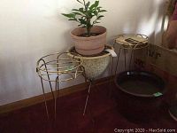 Photo of two gold-tone metal plant stands with a ceramic pot on one stand and a brown plastic pot with a living plant inside the ceramic pot