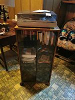 Front view of record player on top of wood-finish glass door cabinet, showing media inside cabinet.
