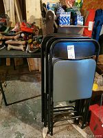 Folded view of four black vinyl folding chairs with metal frames stacked together.