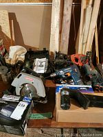 Various power tools and accessories including drills, saws, and chargers on a wooden surface.