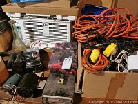 Box containing multiple coiled, orange extension cords beside assorted wood pieces and an air conditioner unit.