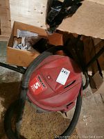 Red Shop-Vac 5 gallon wet-dry vacuum with hose included, shown on rough floor near boxes.