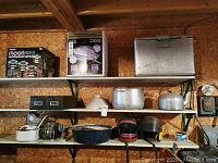 Three shelves with various items: boxed garden lights, silver cooler, pots, kettle, helmets, grinder, and small items.