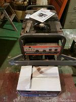 Front view of Craftsman generator on wheels with white cardboard kit box in foreground and operator’s manual on fuel tank