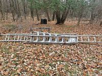 Overview photo showing ladders and sawhorses laid outdoors on fallen leaves under trees.