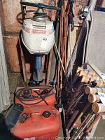 Front view of Evinrude Sportwin motor mounted on wall with steering wheel handle visible above two red fuel tanks on floor