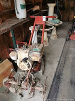 Full view of the rototiller showing the red frame, engine, and blades with soil and debris.