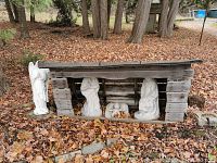 View of the four white stone figures arranged around a wooden rustic shelter outdoors on dried leaves.