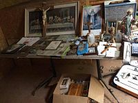  overview of table showing framed and unframed prints, crucifixes, crosses, rosaries, holy water bottle, and box of religious booklets and pamphlets