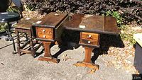 Two pine drop leaf end tables with single drawers, shown outdoors with one table's leaf extended.