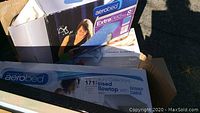 Boxes of Aerobed air mattresses including queen and twin sizes shown outside on pavement with sunlight.