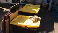 Three plastic bins with yellow lids; the bins hold books and some flat items leaning against them.