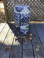 Photo of blue and white ceramic garden stool beside a blue and white ceramic floral pot outdoors on wooden deck.