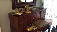 Brass desk accessories arranged on wooden sideboard with mirror showing various items including ink wells and pen holder.