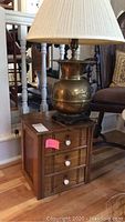 Front of wooden three drawer cabinet with brass lamp on top