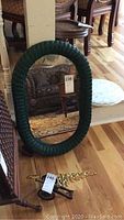 Full view of the green wicker oval mirror leaning against a piece of furniture showing the overall shape and color of the frame.