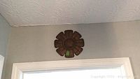 Flower-shaped metal wall art above door frame, dark brown color