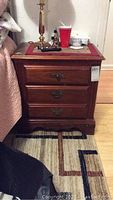 Front view of wooden nightstand showing two drawers with metal handles and items on top, placed next to a bed.
