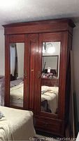 Full view of the antique wardrobe showing its wooden frame, two mirrored doors, and storage drawers underneath