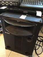 Front view of one black TOA speaker showing horn tweeter and ports, with some wear and labeling on top.