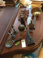 Photo showing 11 items including candle holders, iron stovetop, glass jar, metal lion figure, brass bowl, handheld magnifier on wooden surface
