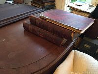 Three large vintage books stacked on wooden table. Books have marbled covers and worn leather spines.