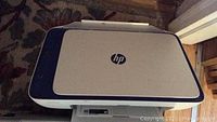 Top view of HP DeskJet 2655 showing white top panel with HP logo and dark blue sides on carpeted floor.