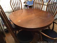 Oval wooden dining table with six chairs around it. Table includes one leaf inserted. Wood finish with visible wear and discoloration spots.
