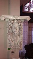 Front angled view of resin wall shelf showing decorative female face and floral elements.