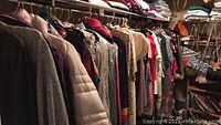 Photo of women's clothing rack with sweaters, jackets, and coats including a grey wool jacket and a light pink quilted jacket