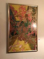 Full view of large framed abstract painting hung on wall with a combination of yellow, green, pink and red colors.