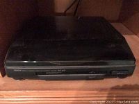 Closed Denon DPR-417 turntable showing front panel and control buttons on wooden shelf.