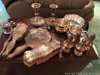 Entire lot arranged on wooden table showing candlesticks, shakers, dresser set, bowls, tray, spoons